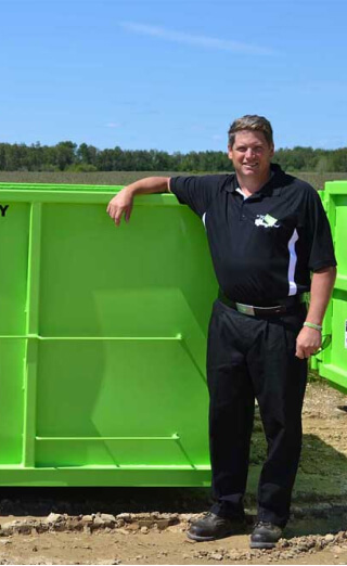 Man standing next to a green dumpster rental franchise outdoors.