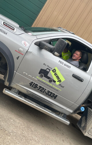 Man sitting in a tilted pickup truck, looking out of the passenger window, part of a junk hauling franchise.